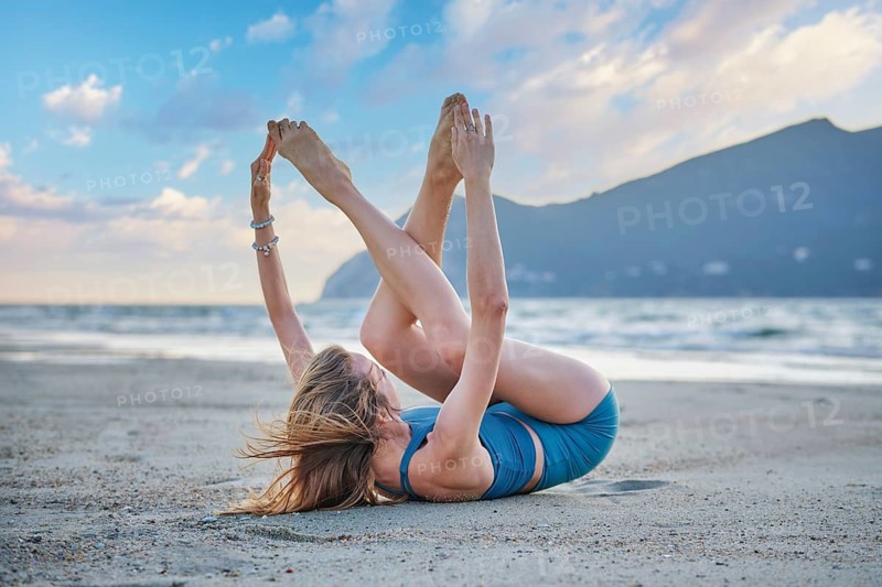 Sandy beach scene featuring ananda balasana, a young woman, happy baby pose, a woman, yoga, and yoga asana