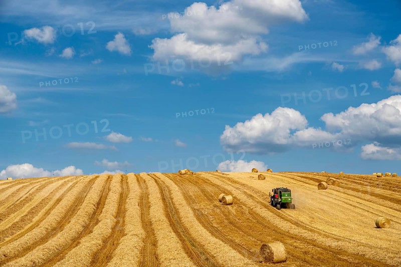 Straw harvest, after harvesting the straw, previously mowed, dried and laid in rows, so-called plumes, is pulled by a round baler, by a tractor, picked up, pressed into compressed bales and placed in the field, used as animal feed, in Mülheim-Menden, Acker an der Mendener Straße, midsummer, harvest at over 30C, Mülheim an der Ruhr, North Rhine-Westphalia, Germany