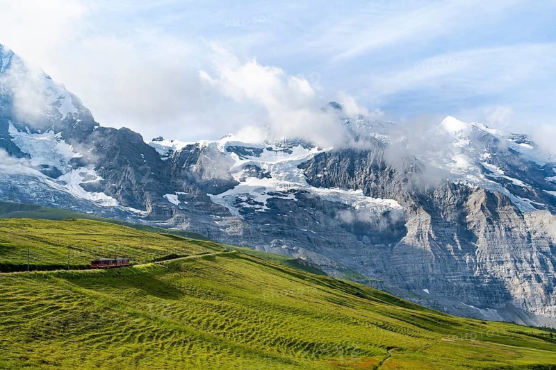 Jungfrau Railway to Jungfraujoch runs through green meadows, above the Kleine Scheidegg stop, rack railway, in the back mountains with peaks Eiger, Mönch and Jungfrau, Jungfrau region, Bernese Oberland, Switzerland