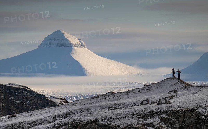 Two people, including a photographer with a stand in front of one of the three mountains Tee Kroner, Kongsfjord or Kongsfjorden, Spitsbergen archipelago, Svalbard, Norway
