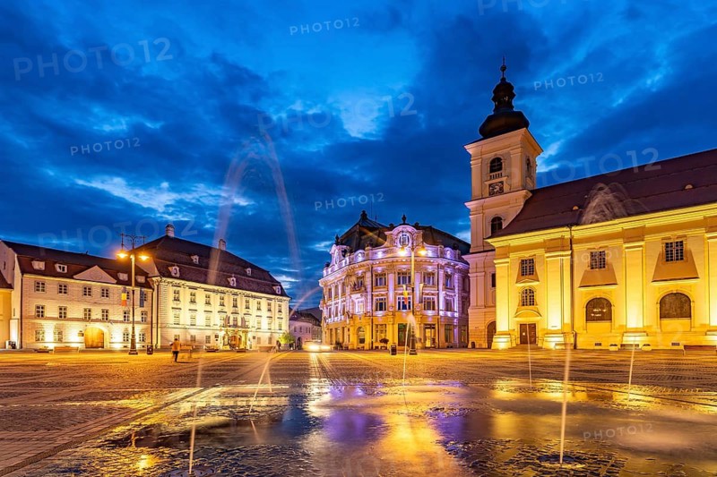 Fountain on Pia?a Mare Great Square, Brukenthal Museum, Sibiu City Hall and the Catholic Parish Church of the Holy Trinity at Dusk, Sibiu or Sibiu, Transylvania, Romania