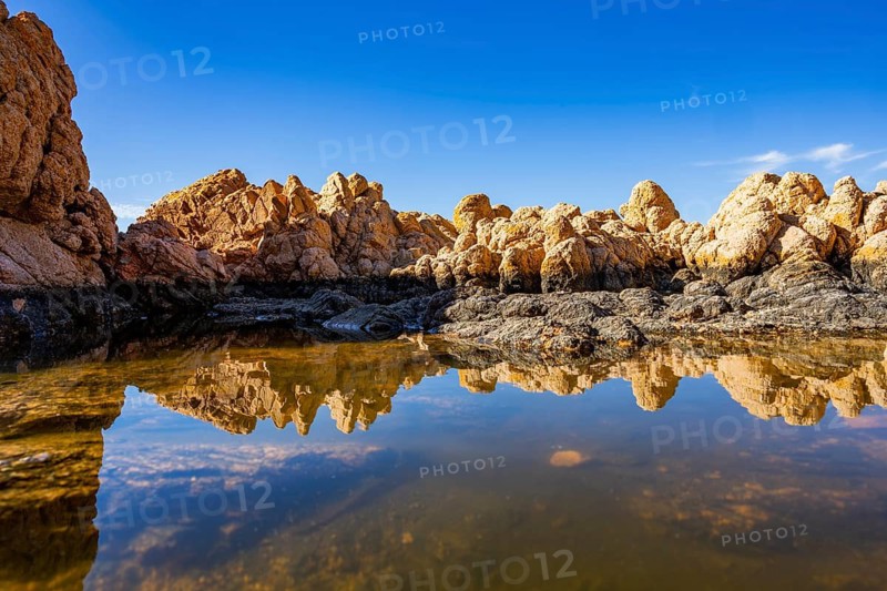 Reflection of stones in a puddle of water from the rocks on the beach at Marinedda Coast on a sunny day, Sardinia, Italy
