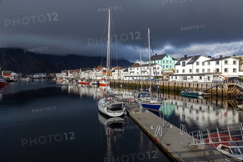 Picturesque harbor with sailboats and traditional wooden houses under dramatic cloudy skies, Henningsvær, Norway