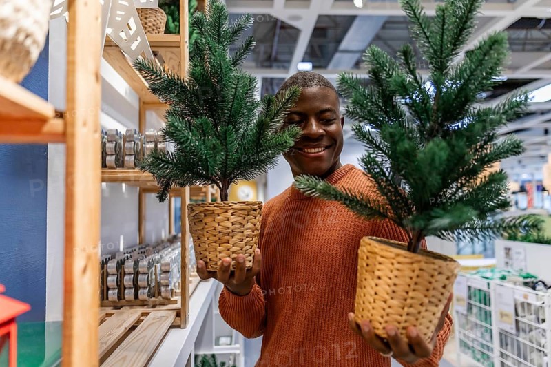 A person is in a store looking at a small Christmas tree. They smile while holding it. The store is decorated for the holiday season