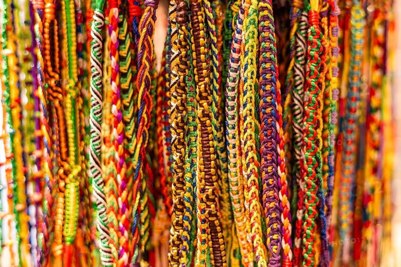 Colorful woven bracelets hang in a display. The intricate patterns feature various bright colors, showcasing craftsmanship and creativity