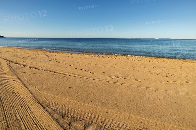 Beach-level viewpoint across raked sand with footprints, calm sea, distant islands, and clear summer sky on Gigaro Beach, La Croix-Valmer, Gigaro Beach, Var, Provence-Alpes-Cote d'Azur, France