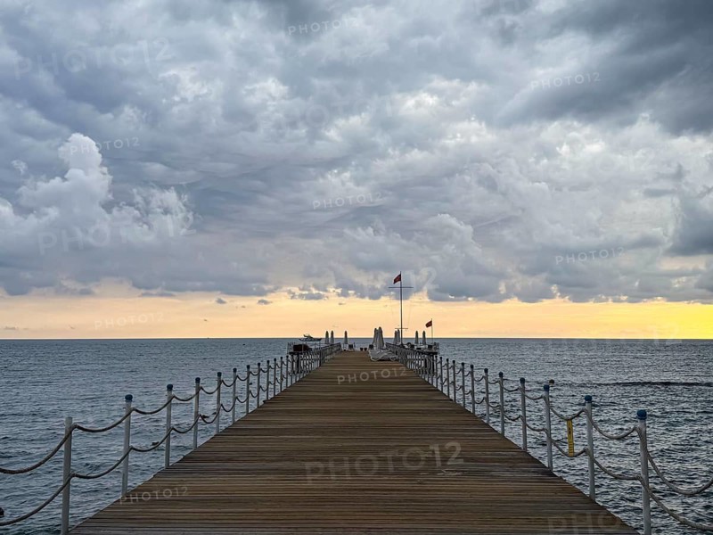 A wooden dock with railing leads into the sea as storm clouds gather in the sky, Side, Manavgat, Antalya Province, Turkey