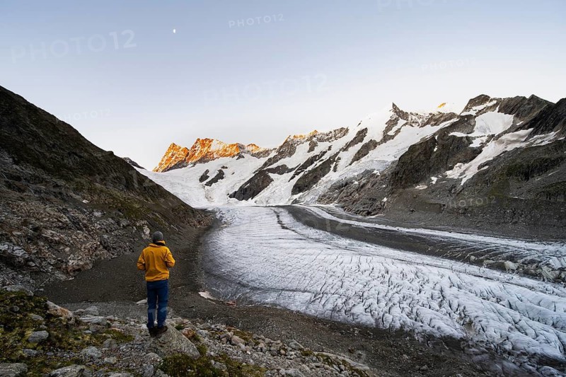Young man in front of impressive high-alpine landscape, Finsteraarhorn and Agassizhorn mountain peaks with alpine glow at sunrise, Upper Arctic Ocean glacier, Bernese Alps, Bernese Oberland, Switzerland