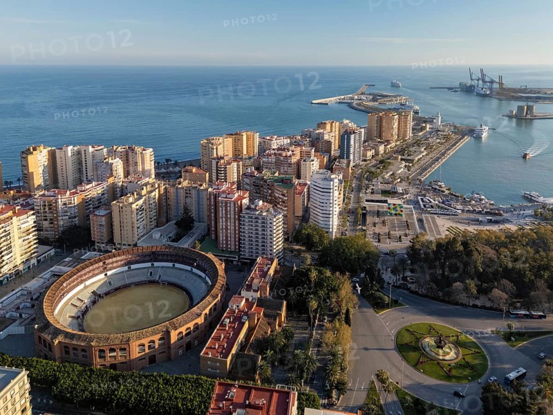 Wide aerial view over Malaga, Spain, showing Plaza de Toros La Malagueta, the dense coastal city, Muelle Uno, harbor basin and Mediterranean port in daylight, featuring port of malaga