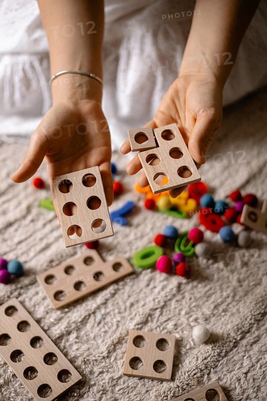 Hands holding wooden counting toys with colorful balls scattered around