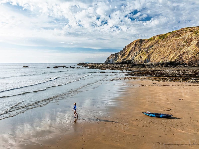 Woman and dog with kayak on Beach from a drone, North Devon and Cornwall Coastpath Border from a drone, Welcombe Mouth Beach, Devon, Cornwall, England, United Kingdom