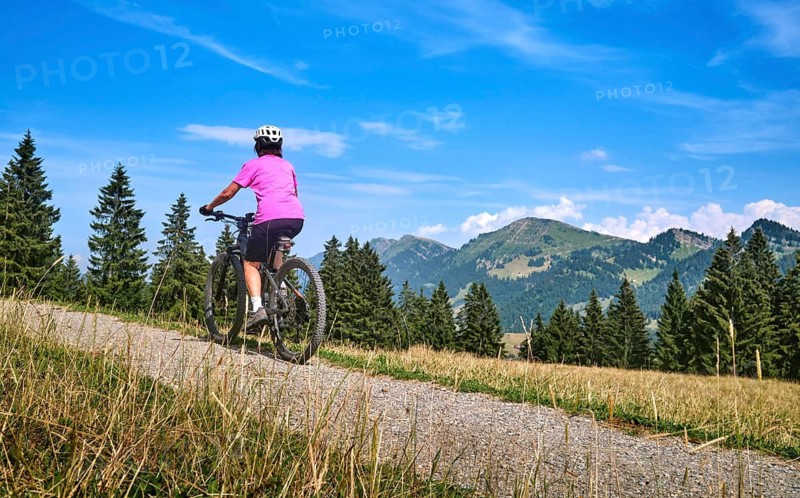Active senior woman rides an e-mountain bike on a picturesque mountain trail under the Nagelfluh Mountains, Oberstaufen, Allgäu, Bavaria, Germany