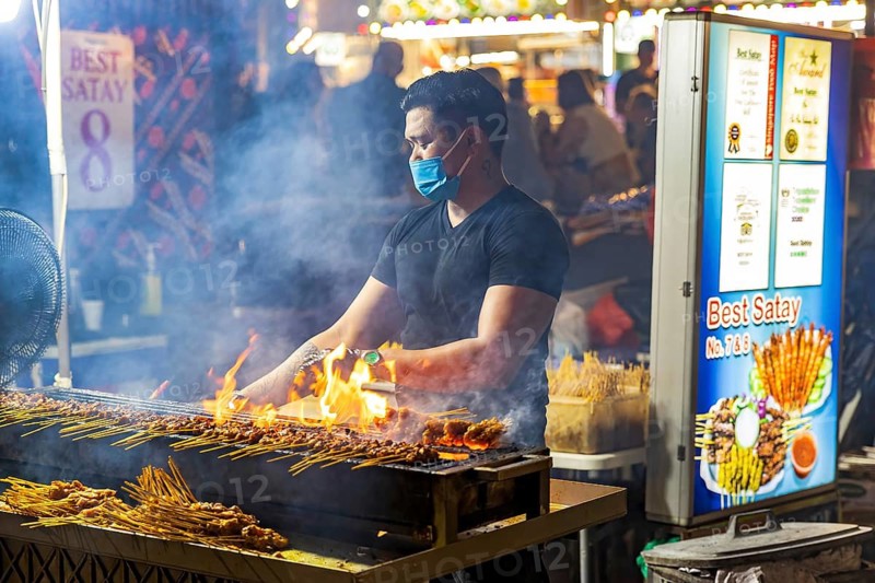 Street food vendor turns and glazes satay skewers over open flames at Satay Street night market, Lau Pa Sat, Singapore