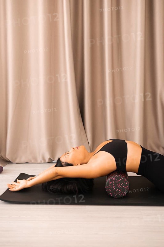 Woman in a relaxed stretching position on a foam roller with a calm and neutral background