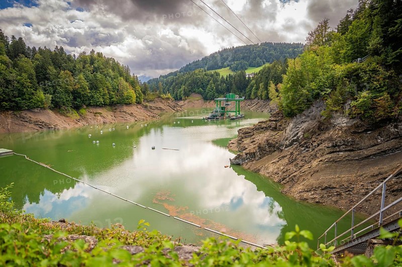 View of green lake surrounded by thick forests, cloudy sky, Krumbach, Vorarlberg, Austria