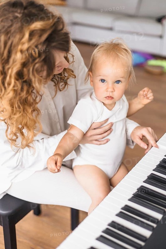 A mother lovingly holds her baby at the piano, engaging in a nurturing interaction