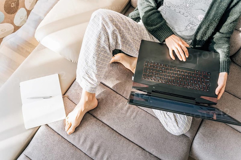 A woman in home clothes with a laptop, next to her is a notebook and a pen, Person working on a laptop while sitting on a couch, with a notebook and pen nearby, creating a relaxed and cozy atmosphere