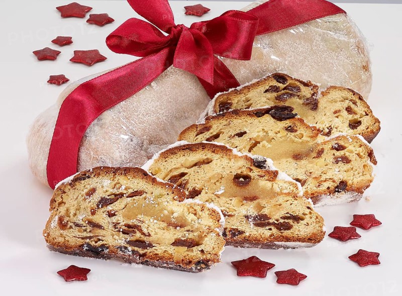 Christmas stollen wrapped and decorated with red ribbon, in front of 4 slices of stollen, red stars as decoration, studio shot