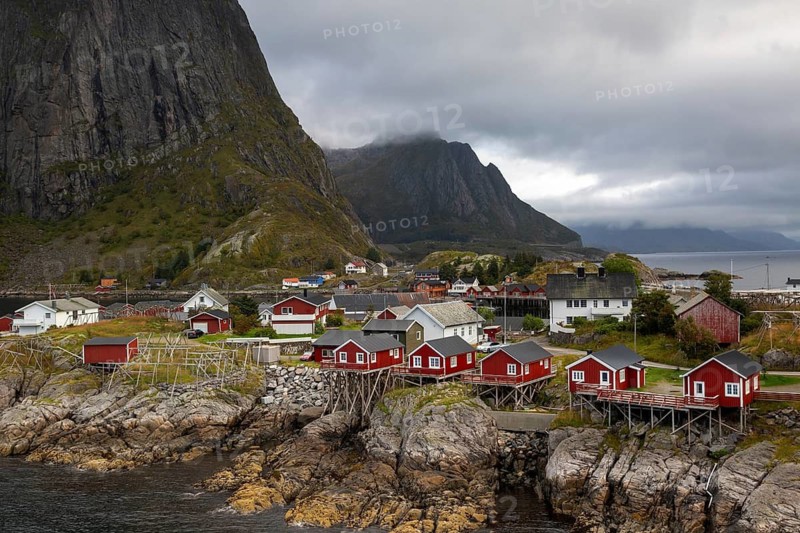 Picturesque fishing village Hamnøy with red Rorbuer huts on rocky cliffs against steep mountain walls under cloudy sky, Hamnøy, Lofoten, Norway