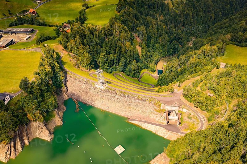 View of dam and green water surface, surrounded by forest and agricultural buildings, Krumbach, Vorarlberg, Austria