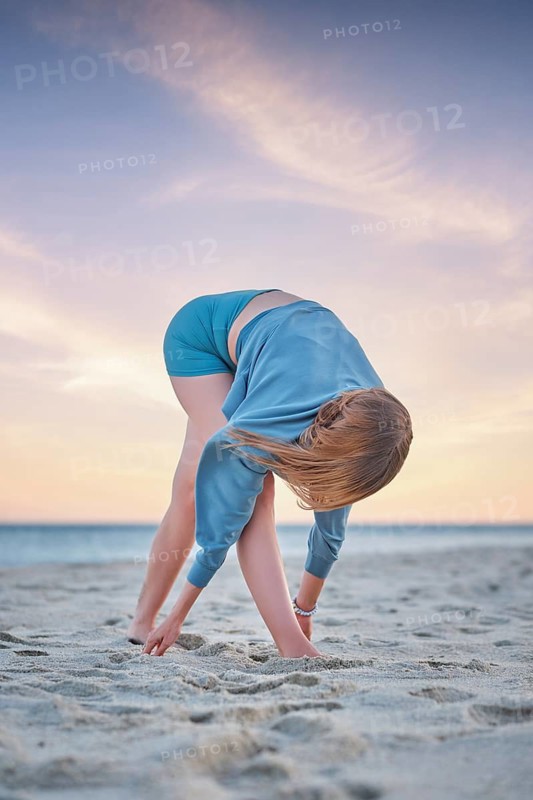 Beach scene featuring a woman, yoga, prasarita padottanasana, wide leg fold, forward bend, and forward fold