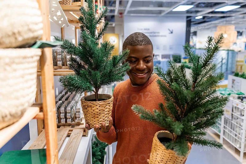 A smiling African American with a Christmas tree in his hands in store.