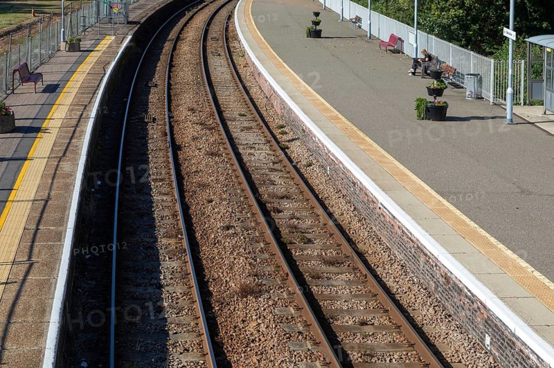 Person sitting on platform bench waiting for train, oblique overhead view of railways tracks, Beccles, Suffolk, England, UK