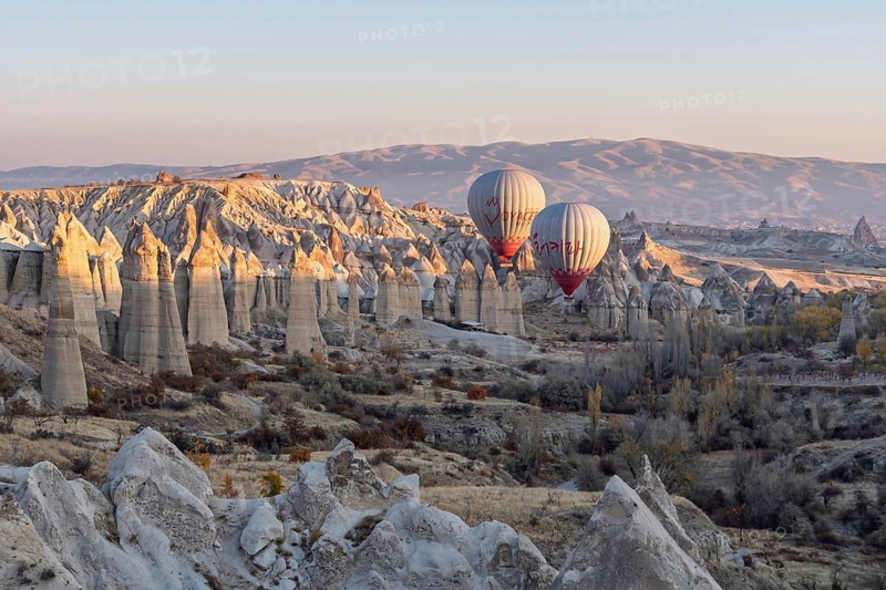 Hot air balloons float over a picturesque rocky landscape in soft morning light, Cappadocia, Turkey