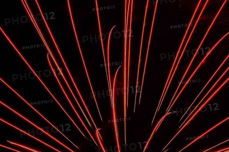 Orange and red illuminated trailing streaks of fireworks in black sky at night in summer, Quebec, Canada