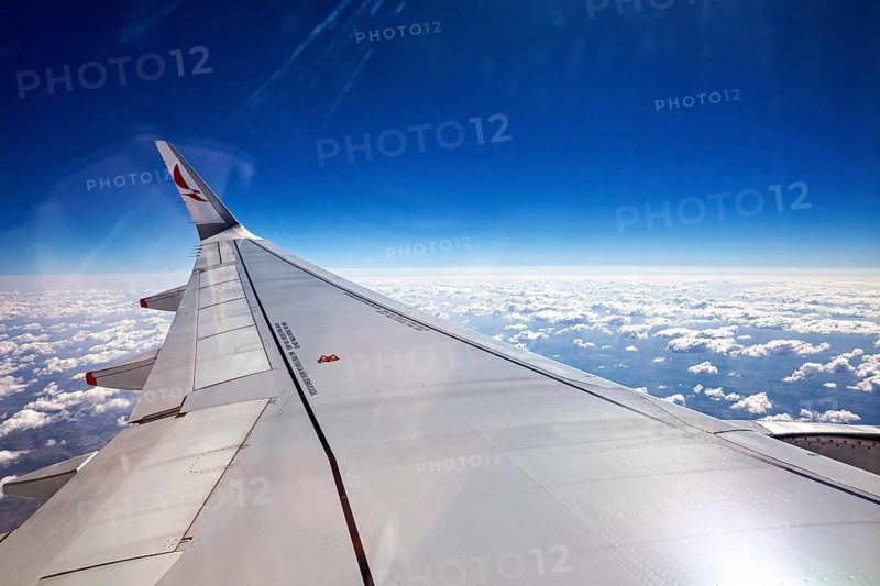 View from an airplane window with a view of the wing and many clouds under a blue sky, aircraft wings above the clouds
