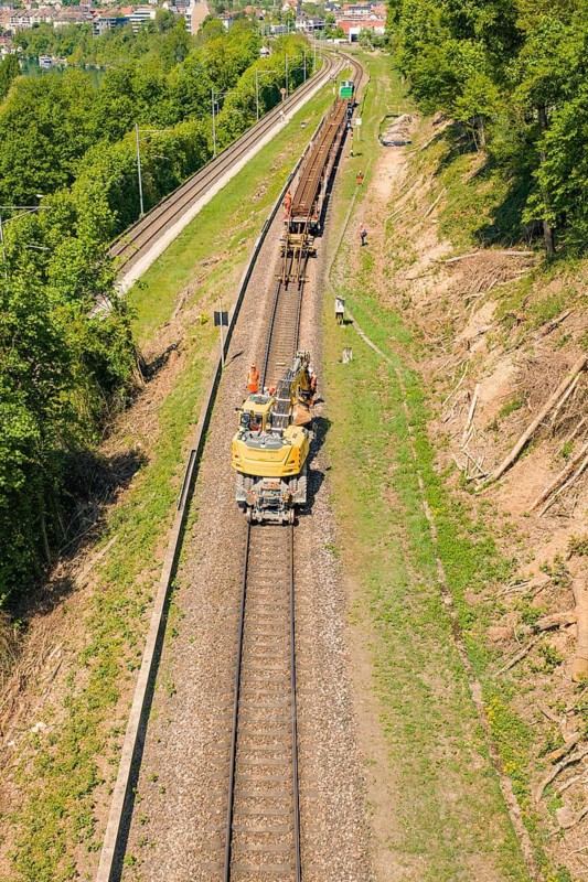 Vehicle and workers seen on a sunny train line in green surroundings, Leonhard Weiss construction site to renovate the station and build the overhead line, Waldshut, Germany