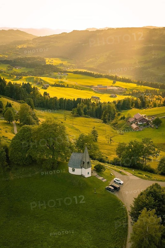 Aerial view of picturesque hilly landscape with small chapel in sunlight, Bruder Klaus chapel, Allgäu, Bavaria, Germany