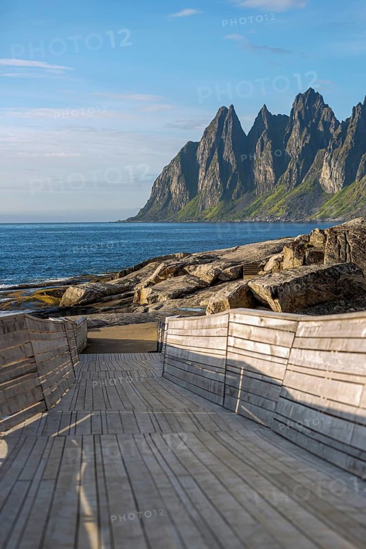 Modern wooden walkway leads to the rocky coast of Tungeneset in front of the distinctive Devil's Teeth, Senja Island, Norway