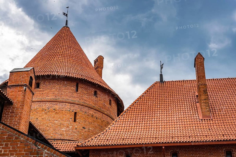 View of the red tiled roof and red brick masonry of the towers of Trakai Castle, Trakai, Lithuania, Medieval brick castle with red roofs and towers under a cloudy blue sky