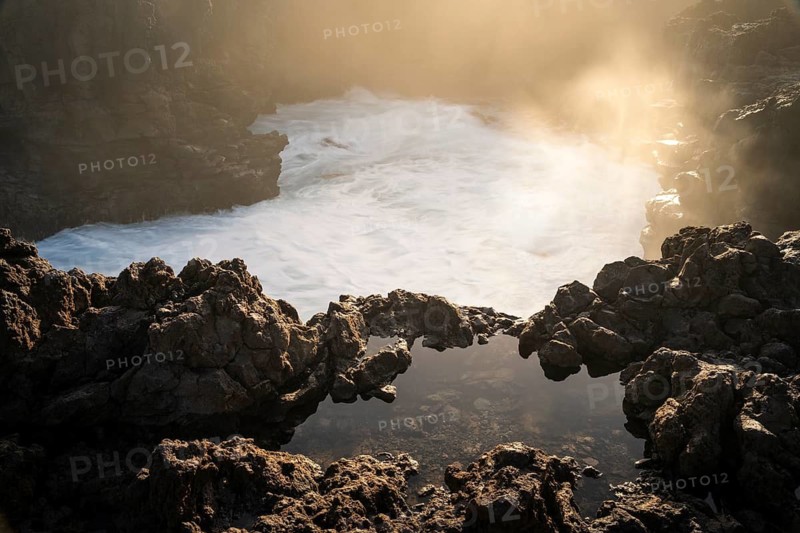 Seawater collects in a small pool, spray rises in the backlight. In the morning. La Fajana, La Palma, Canary Islands, Spain