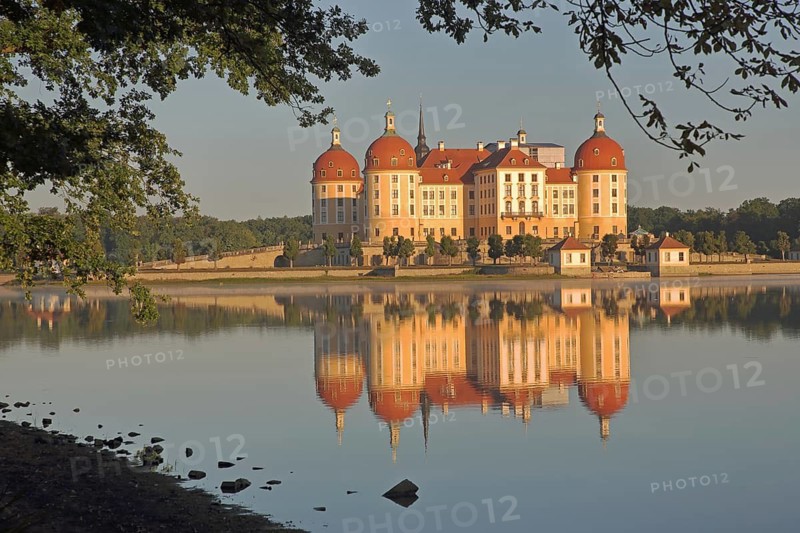 Baroque castle with reflection in lake and shore, yellow baroque castle with corner towers, lighting atmosphere, Moritzburg, Saxony, Germany