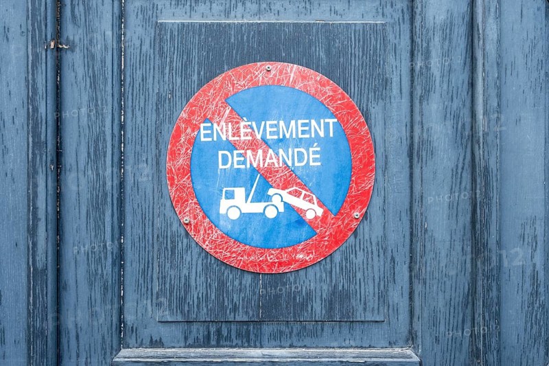 Round, red-blue parking sign with the inscription ENLÈVEMENT DEMANDÉ and a tow truck symbol on a weathered, blue-painted wooden door with vertical grain, Paris, Département Paris, Île-de-France, France