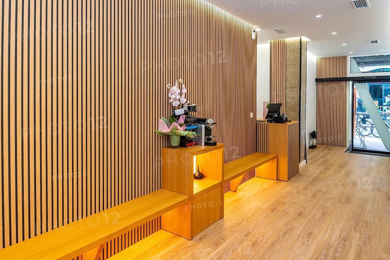 Contemporary aesthetic clinic reception with warm wooden slat wall panels, integrated seating and subtle lighting for a clean, minimalist, welcoming spa and wellness waiting area