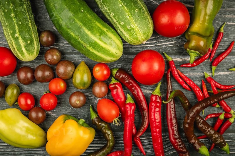 Fresh, colorful vegetables such as cucumbers, tomatoes, peppers, hot peppers on dark wood