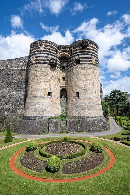 Monumental castle complex from the 13th century with distinctive tower architecture, nestled in a well-kept park and garden landscape with symmetrical patterns in the deep ditch in front of the fortress walls, Château d'Angers, Angers, Maine-et-Loire, Pays de la Loire, France