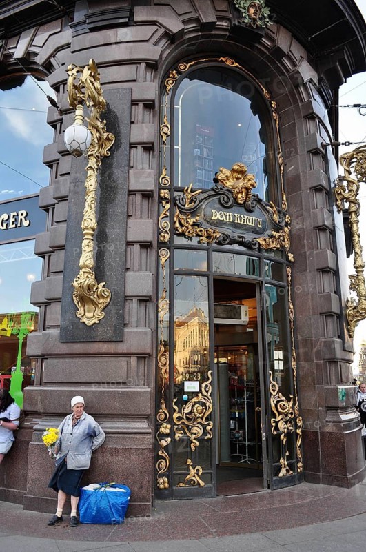 Magnificent building with golden elements in the city, in front of it a woman with flowers, Singer House, St. Petersburg, Russia
