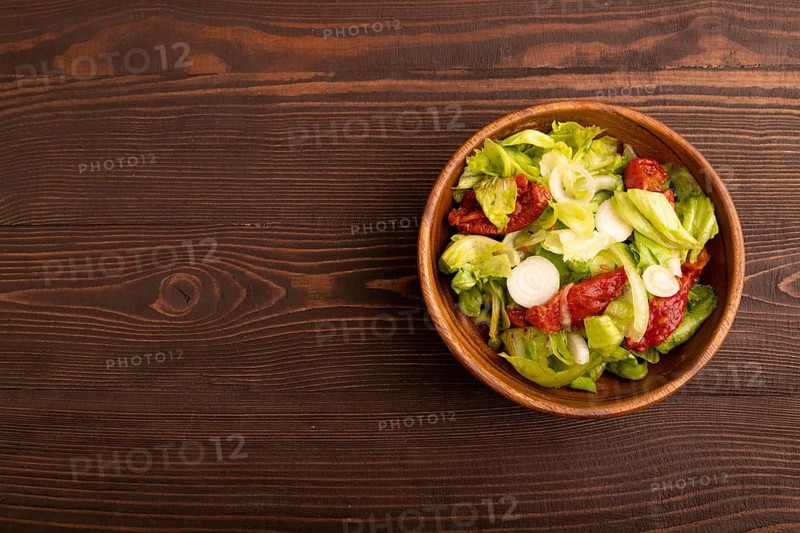 Mixed salad with lettuce, tomatoes, onion and vegetables in wooden bowl on brown wooden background. top view, flat lay, copy space