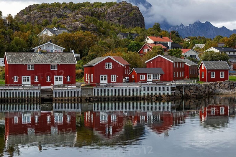 Traditional red Rorbuer fishing huts on the water with perfect reflection against wooded slopes and mountains, Norway