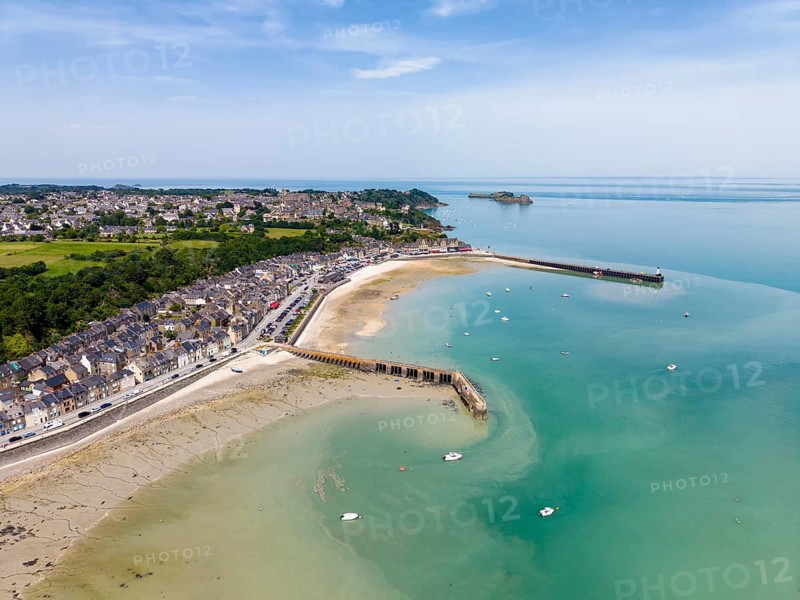 Aerial view of the picturesque fishing village of Cancale on the Emerald Coast. The picture shows the Port de la Houle harbour area at low tide with the distinctive Cale de l'Épi pier. The row of houses with numerous fish restaurants stretches along the shore. The region is world-famous for its oyster farming. In the background you can see Mont-Saint-Michel Bay, Ille-et-Vilaine department, Brittany, English Channel, France