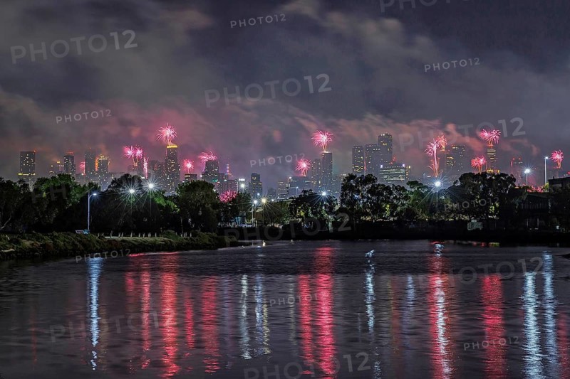 City skyline with fireworks lighting up the night sky, reflections on the river, Fireworks from the rooftop of buildings in the city centre welcome in the New Year, Melbourne, Victoria, Australia
