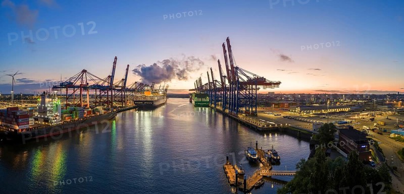 Panoramic aerial view at Waltershof harbour during the Blue Hour with Eurogate Container Terminal Hamburg (CTH) and Container Terminal Burchardkai (CTB) with the brightly lit Ever Meed, Manila Express and Fort Desaix in the background, Hamburg, Germany