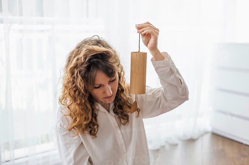 A woman with curly hair holding a wooden chime in a softly lit room