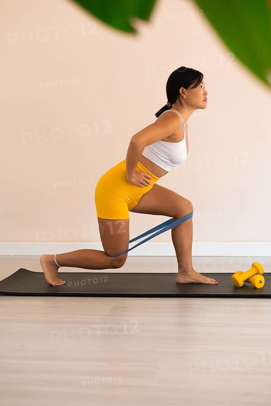 A woman exercising with a resistance band on a yoga mat in a simple, bright space