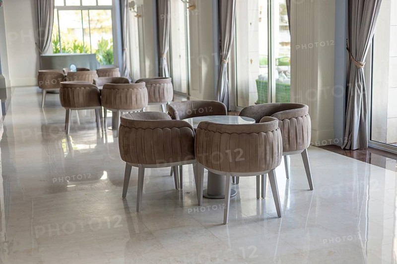 Modern interior of a cafe with round tables and plush chairs. Large windows allow natural light to fill the space, creating a welcoming atmosphere