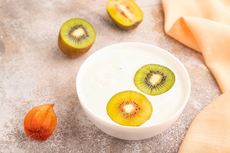 Yogurt with kiwi in white bowl on brown concrete background and orange linen textile, side view, close up, minimalism